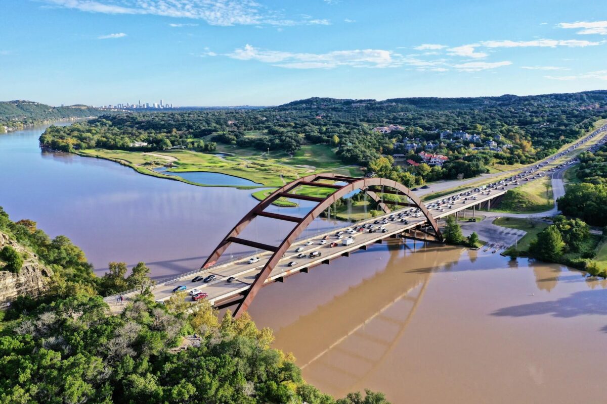 Cars drive over the Pennybacker bridge during rush hour with a view of the Austin skyline.